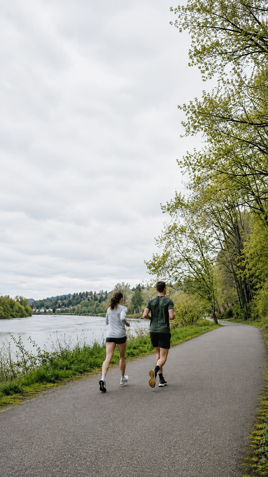 Two runners on a riverside path, moving away from the viewer